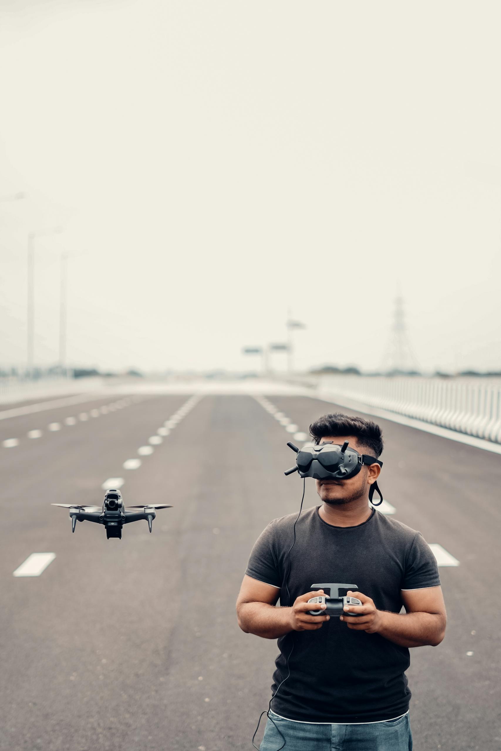 A young man using a drone and VR goggles on an open road showcasing advanced technology.